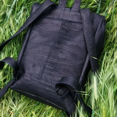 Rucsac laptop din piele nabuc negru KC Wabi-Sabi, așezat pe iarbă, vedere din spate din unghi lateral