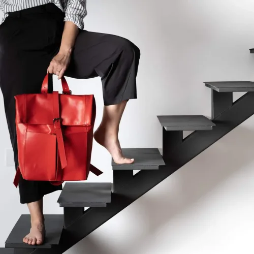 Rucsac laptop din piele naturală roșie Wabi-Sabi, ținut de model de mâner, pe scări, vedere frontală