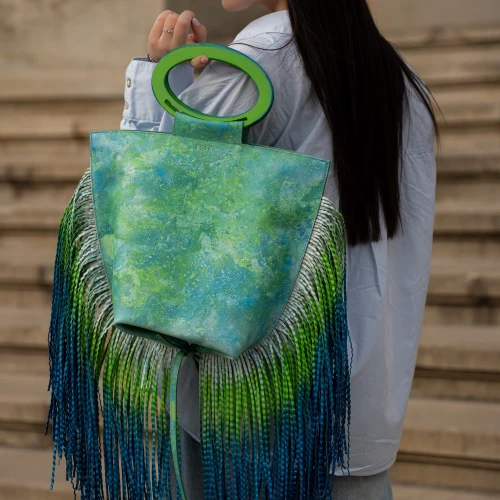 Geantă KOJA cu franjuri lungi, purtată pe umăr, în nuanțe de verde-albastru, fotografiată în ținută casual.