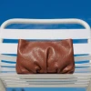 Clutch Inanna din piele naturala maro tabac, asezat pe un scaun alb, pe fundal albastru